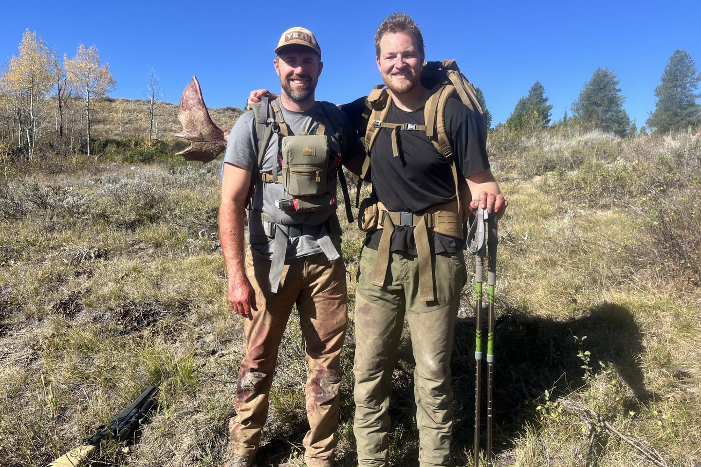 Two hunters with loaded pack frames during a moose pack out, an antler visible over one shoulder
